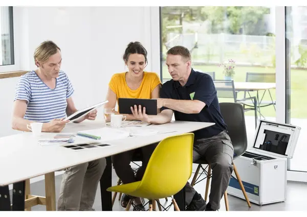 Drei Personen besprechen eine Energieberatung mit Tablet und Unterlagen am modernen Tisch.