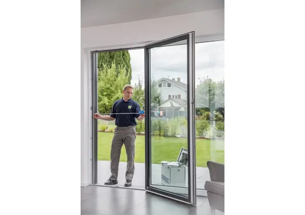 Ein Handwerker misst eine große Terrassentür aus Glas in einem modernen Wohnzimmer aus.