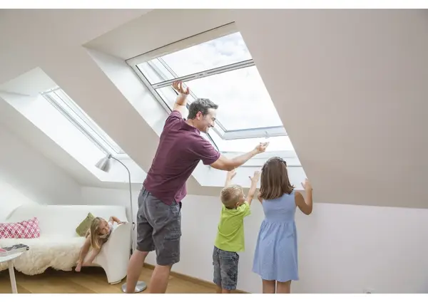 Vater mit zwei Kindern öffnet Dachfenster im hellen, modernen Dachgeschosswohnzimmer.