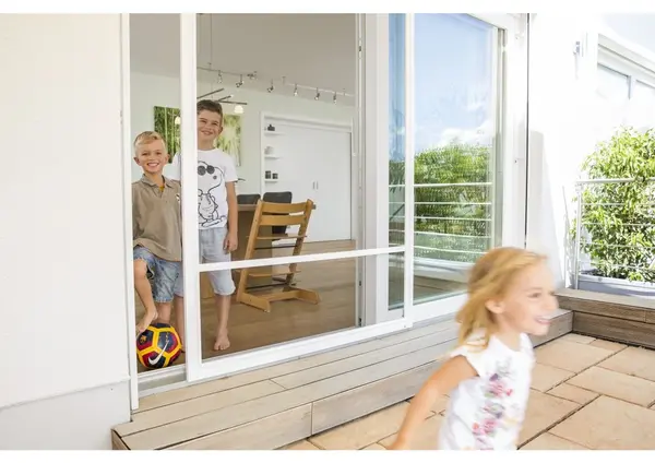 Kinder spielen vor einer modernen Terrassentür mit Insektenschutz im sonnigen Garten.